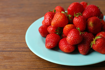 Ripe strawberries in plate on wooden background