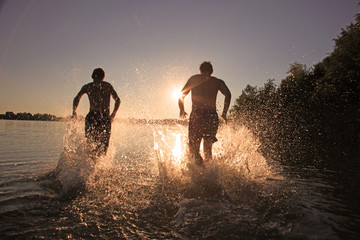 Glückliche junge Menschen laufen und springen am See beim Sonnenuntergang