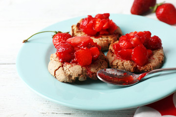 Cookies with fresh strawberry in plate on wooden table, closeup