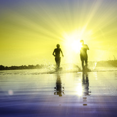 Glückliche junge Menschen laufen und springen am See beim Sonnenuntergang