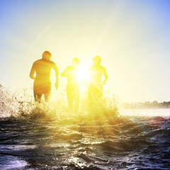 Glückliche junge Menschen laufen und springen am See beim Sonnenuntergang