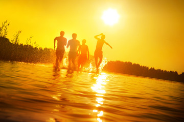 Glückliche junge Menschen laufen und springen am See beim Sonnenuntergang