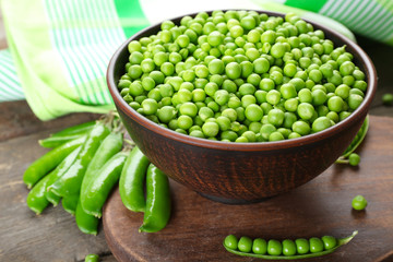 Fresh green peas in clay bowl on wooden cutting board, closeup