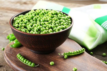 Fresh green peas in clay bowl on wooden cutting board, closeup