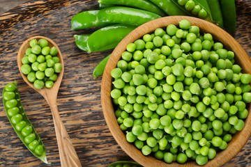 Fresh green peas in bowl on wooden tray, top view