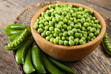 Fresh green peas in bowl on wooden tray, closeup