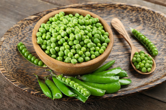 Fresh green peas in bowl on wooden tray, closeup