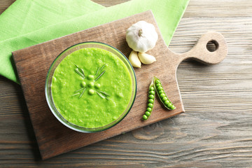 Green pea soup in glass bowl on wooden cutting board, top view