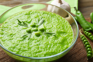 Green pea soup in glass bowl on wooden cutting board, closeup