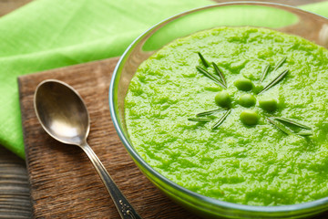 Green pea soup in glass bowl on wooden cutting board, closeup