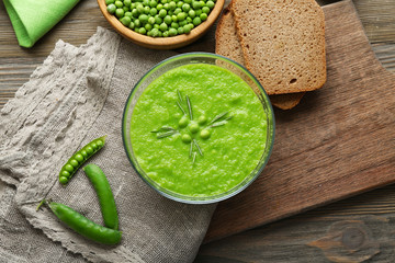 Green pea soup in glass bowl on wooden cutting board with sackcloth, top view