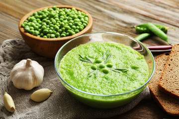 Green pea soup in glass bowl on wooden cutting board with sackcloth, closeup