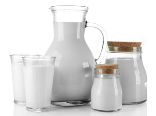 Pitcher, jars and glasses of milk on wooden table, on white background