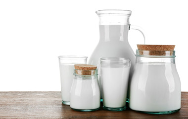 Pitcher, jars and glasses of milk on wooden table, on white background