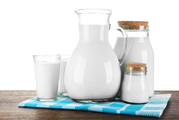 Pitcher, jars and glasses of milk on wooden table, on white background