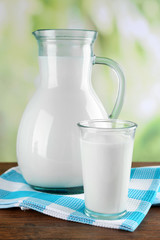 Pitcher and glass of milk on wooden table, on nature background