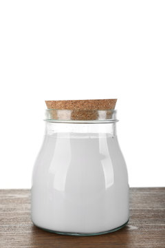 Glass jar of milk on wooden table, on white background