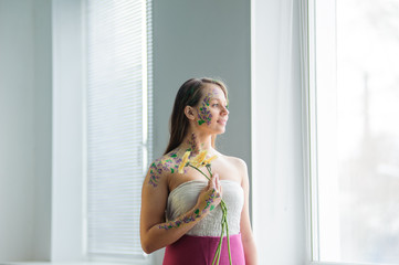 Girl with flower bodyart and sunflowers bouquet and wreath near window