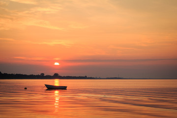 Fototapeta premium Boat in the ocean with the sun rising behind it