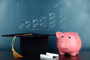 Piggy bank with grad hat on blackboard background