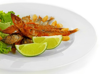 Fried small fish with lettuce and lime on plate close up