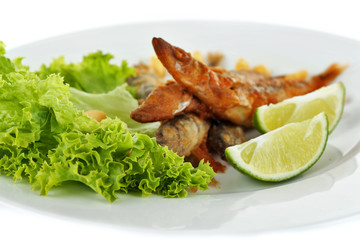 Fried small fish with lettuce and lime on plate close up