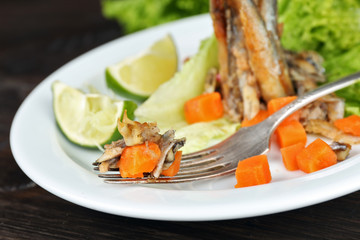 Fried small fish with carrot and greens on table close up