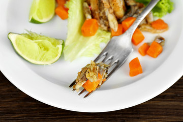Fried small fish with carrot and greens on table close up