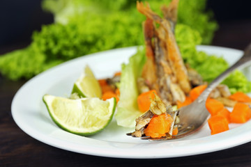 Fried small fish with carrot and greens on table close up