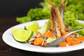 Fried small fish with carrot and greens on table close up