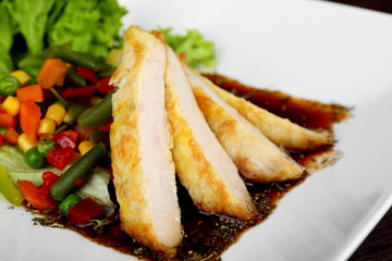 Slices of chicken fillet with sauce and vegetables on plate close up