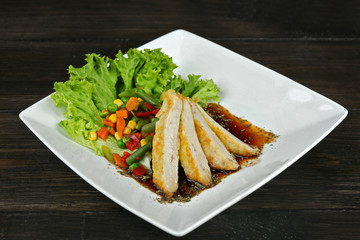 Slices of chicken fillet with sauce and vegetables on table close up