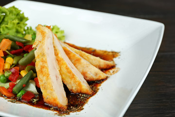 Slices of chicken fillet with sauce and vegetables on table close up