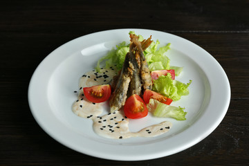 Fried small fish with vegetables on table close up