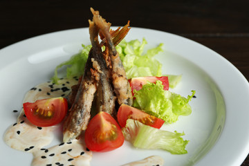Fried small fish with vegetables on table close up