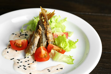 Fried small fish with vegetables on table close up