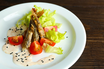 Fried small fish with vegetables on table close up