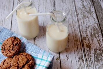 Horizontal shot of some chocolate cookies and two glasses of milk on a rustic table
