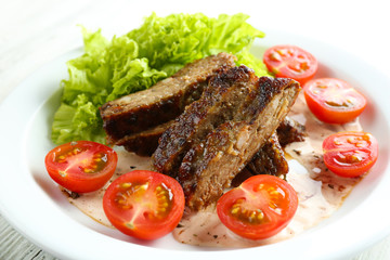 Tasty slices of meat with sauce and cherry tomato on plate close up