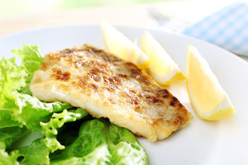 Dish of fish fillet with lettuce and lemon on table close up