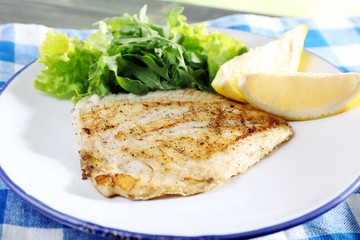 Dish of fish fillet with lettuce and lemon on table close up