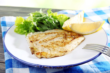 Dish of fish fillet with lettuce and lemon on table close up