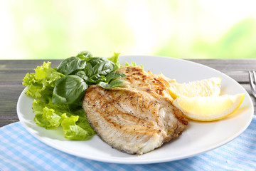 Dish of fish fillet with greens and lemon on bright background