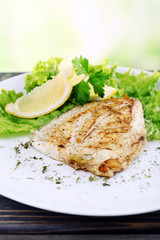 Dish of fish fillet with greens and lemon on bright background