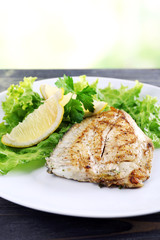 Dish of fish fillet with greens and lemon on bright background