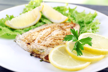 Dish of fish fillet with lettuce and lemon on plate close up