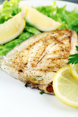 Dish of fish fillet with lettuce and lemon on plate close up