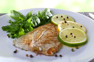 Dish of fish fillet with greens and lime on table close up