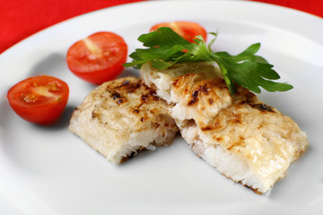 Dish of fish fillet with parsley and tomato on plate close up
