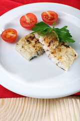 Dish of fish fillet with parsley and tomato on plate close up